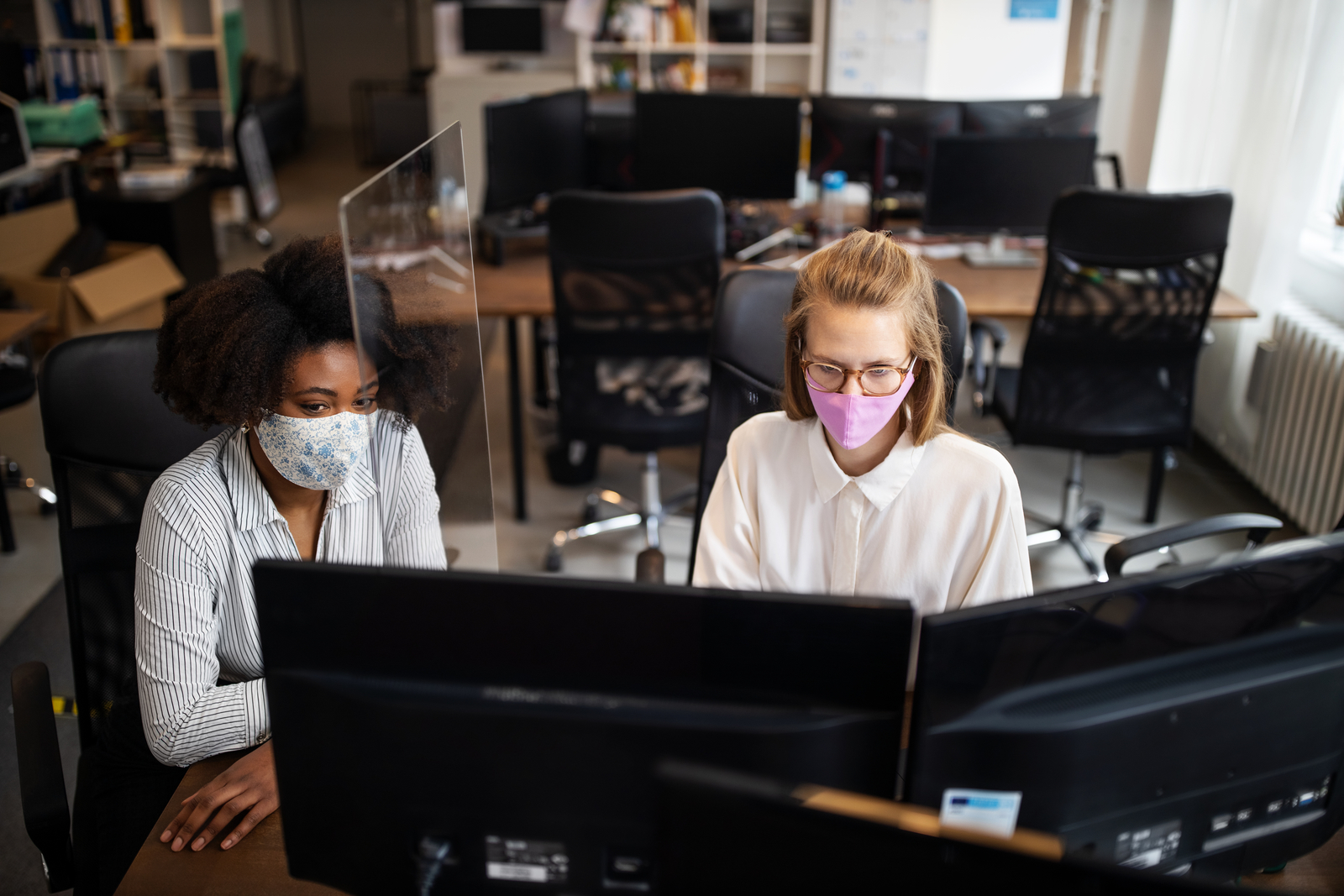 Businesswomen wearing face mask working together with a glass partition at office