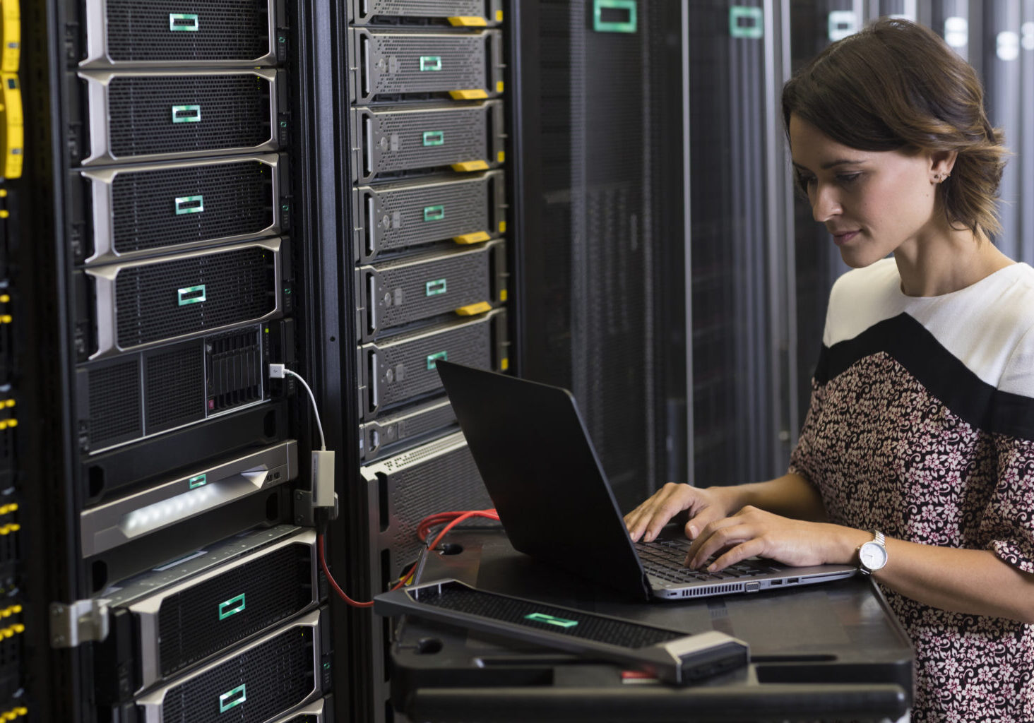 Woman using a laptop to work on a server rack